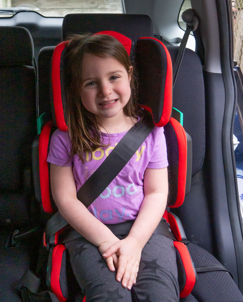 young girl in red hifold travel highback booster seat