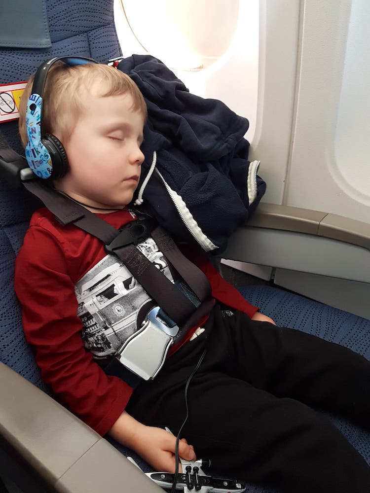 Boy in red sweater asleep while restrained with the CARES toddler airplane seatbelt