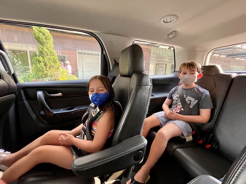 Travel Car Seat Expert - Two children sitting in the back seat of a car wearing face masks while using a travel car seat.