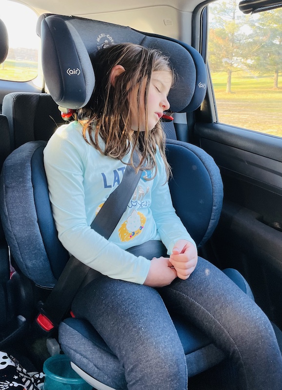 School age girl in turquoise shirt asleep in dark blue Maxi Cosi RodiFix booster seat for car sleeper.