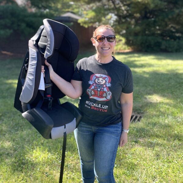 Travel Car Seat Expert - A woman standing next to a car seat in a grassy area, checking out the best travel car seat option for her upcoming trip by plane.