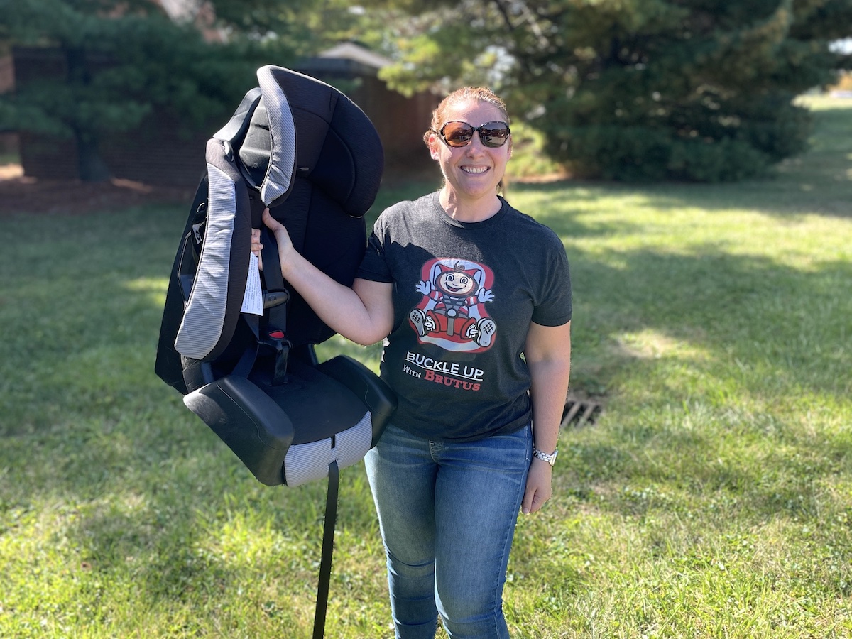 Travel Car Seat Expert - A woman standing next to a car seat in a grassy area, checking out the best travel car seat option for her upcoming trip by plane.