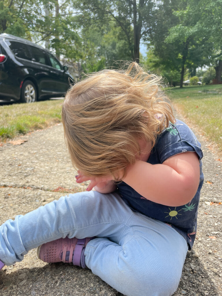 Travel Car Seat Expert - A little girl sitting on the sidewalk with her hands on her face.