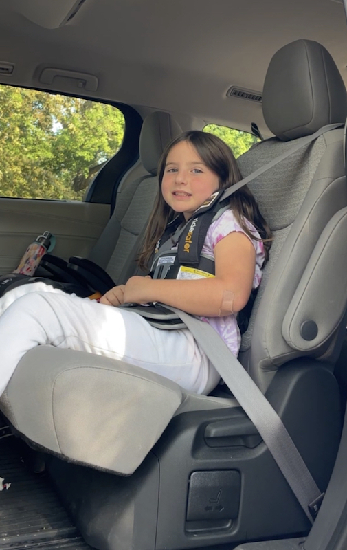 Travel Car Seat Expert - A young girl wearing the Ride Safer Travel Vest sits comfortably in the back seat of a car.