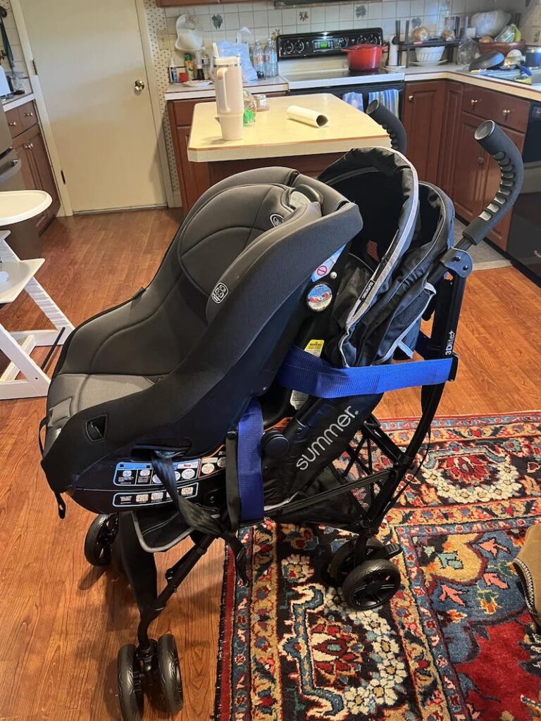 Travel Car Seat Expert - A baby car seat is secured onto a folding stroller in a kitchen with wooden floors and a patterned rug.